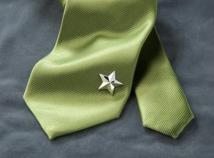 Produktfotografie eines Schmuckstückes in Form eines Sterns, welcher am Ende einer grünen Krawatte befestigt ist.