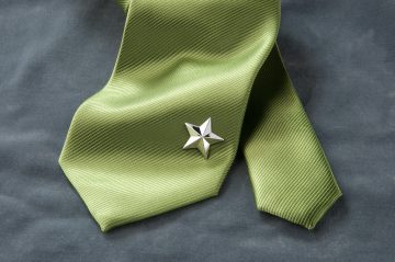 Produktfotografie eines Schmuckstückes in Form eines Sterns, welcher am Ende einer grünen Krawatte befestigt ist.