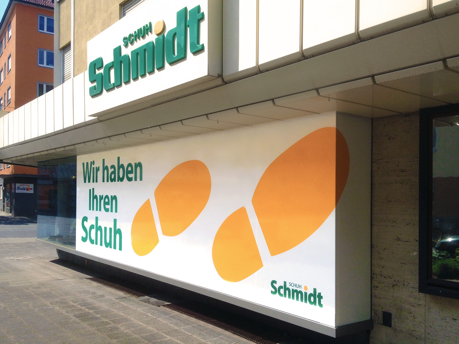Sichtschutzbeklebung für das Schuhgeschäft Schuh Schmidt in einem Schuhabdruckdesign auf weißem undurchsichtigen Grund und grüner Schrift aus Plotbuchstaben.
