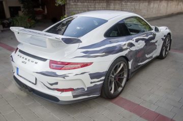Weißer Porsche GT 3 mit grauer Folienbeklebung in einer zerissenen Optik von schräg hinten.