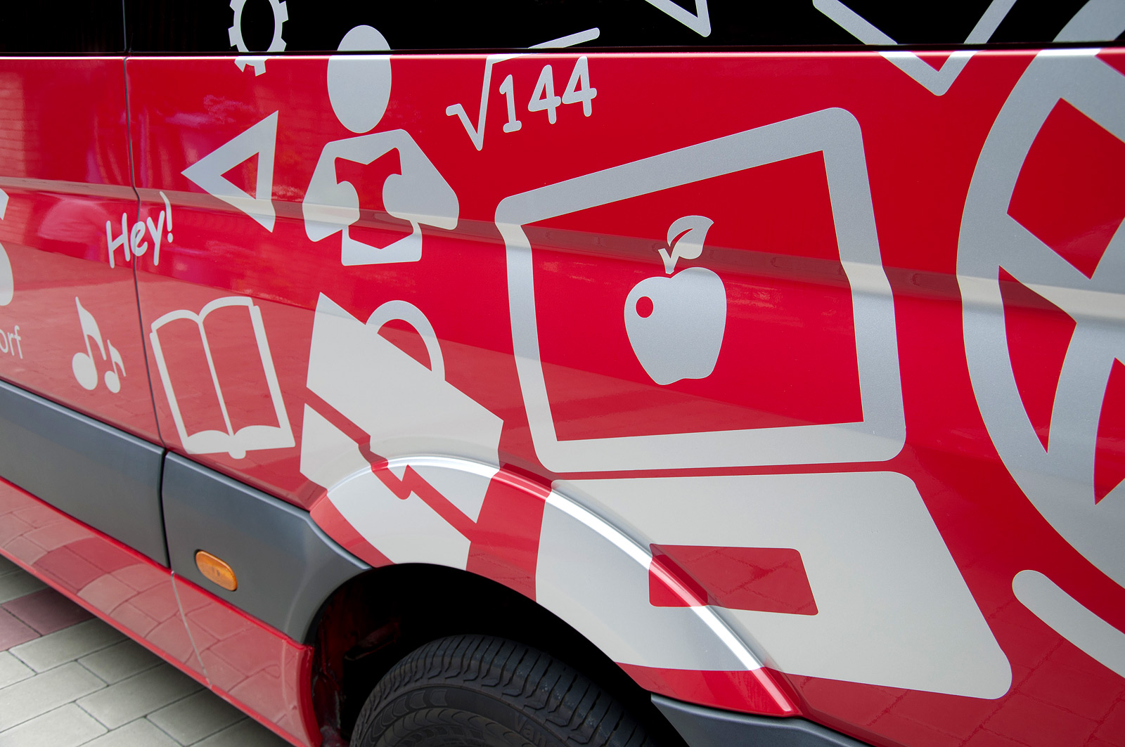 Eine Nahaufnahme des linken hinteren Teils des roten Schulbusses der Gemeinde Rückersdorf der mit verschiedenen grauen Symbolen beklebt wurde.
