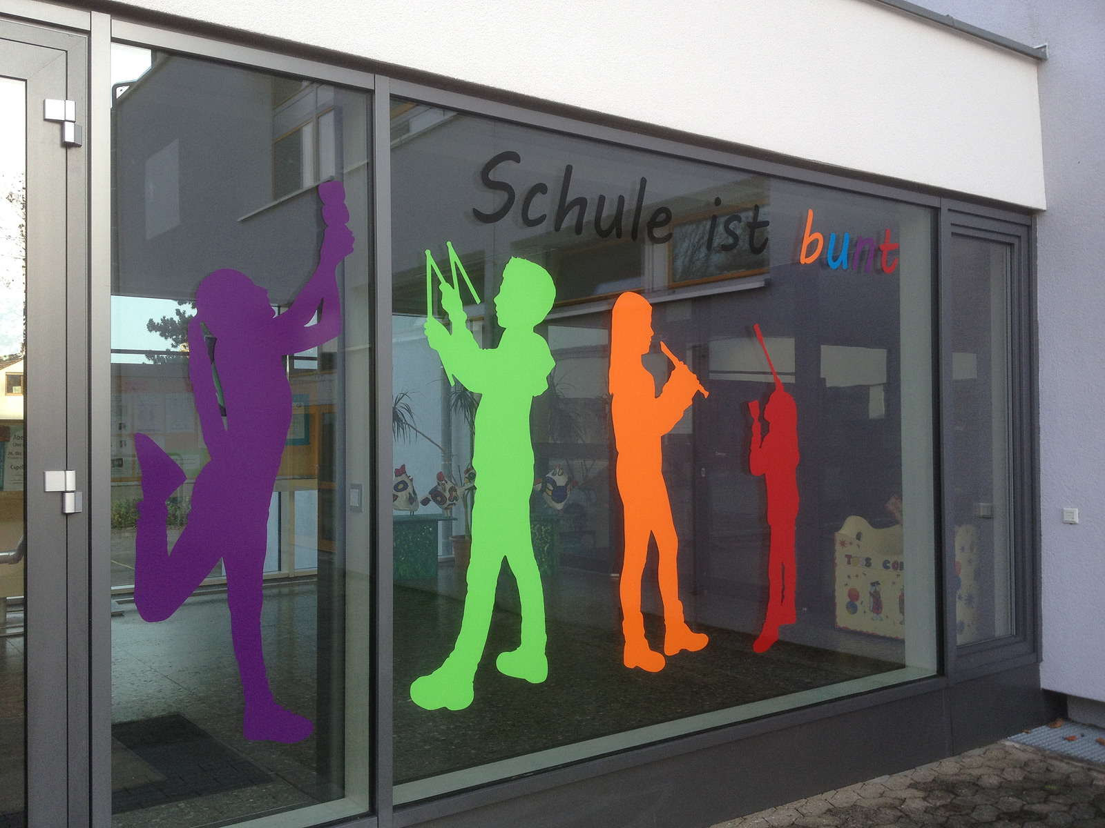Fensterbeschriftung an der Grundschule in Oberasbach: Mehrere Figurensilhouetten und Schrift in verschiedenen bunten Folie.