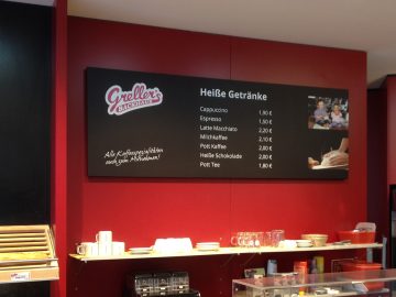 Sicht auf ein Preisschild in Tafeloptik der Bäckerei "Greller's Backhaus" mit weißer Folienschrift und Fotodrucken.