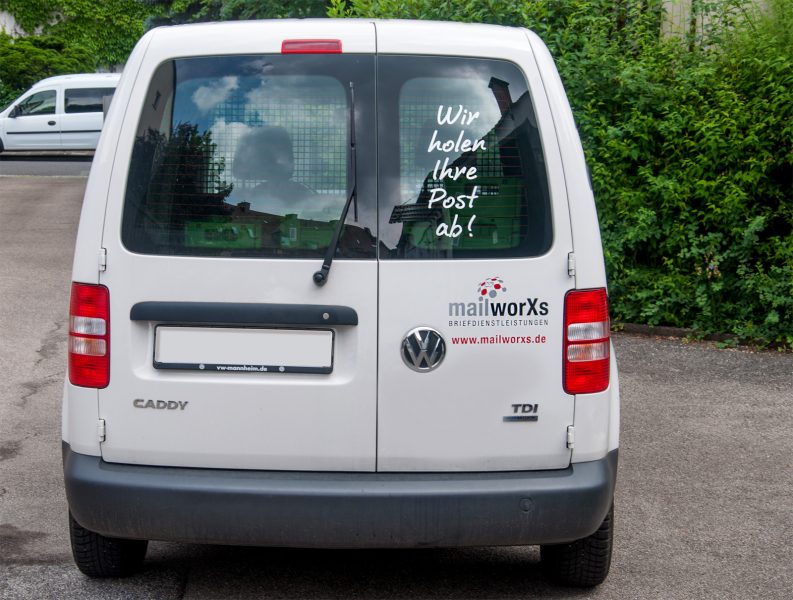 Heckansicht des folierten MailxorXs Fahrzeuges Caddy mit dem Slogan "Wir holen Ihre Post ab!"