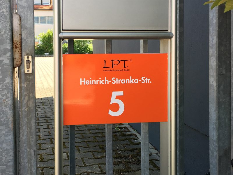 Orangefarbenes Schild mit Straßenname und Hausnummer